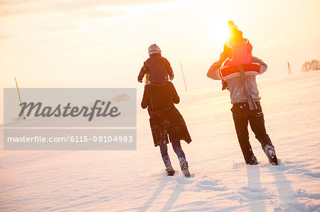 Parents carrying children on shoulders in snowy landscape