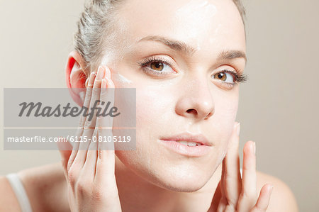 Young woman applying lotion on face, close-up