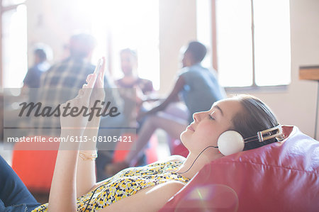 Casual businesswoman relaxing with headphones and digital tablet on bean bag chair