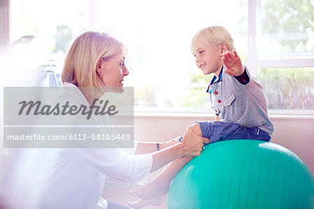 Physical therapist holding boy with arms outstretched on fitness ball