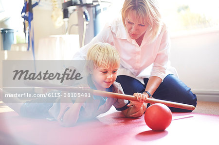 Physical therapist guiding boy rolling ball with stick