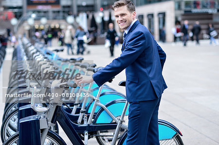 Smiling businessman take his bicycle from parking