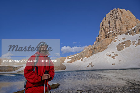 Woman is pleased with mountain travel. Rocks with snow and blue sky are in the background.