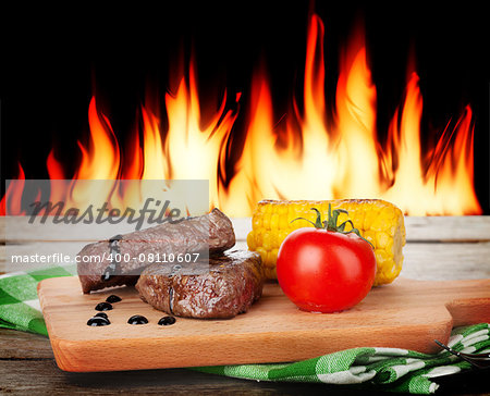 Steak with grilled vegetables on wooden table and fireplace