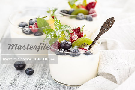 Fresh yogurt with berries. On white rustic table. Focus on mint leaves and kiwi and blueberry in the center of the first glass.