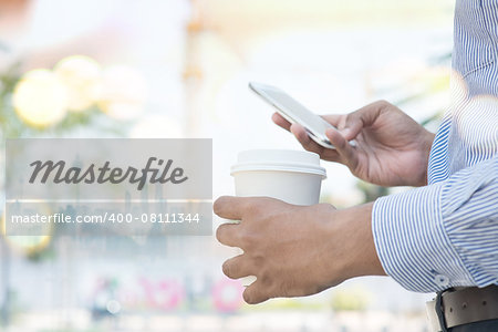 Man hand holding take away coffee cup while using smartphone, outdoors business concept.