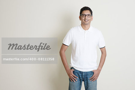 Front view portrait Indian guy standing on plain background with shadow and copy space.