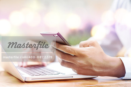 Asian Indian businessman using smartphone and laptop computer at outdoor cafeteria.