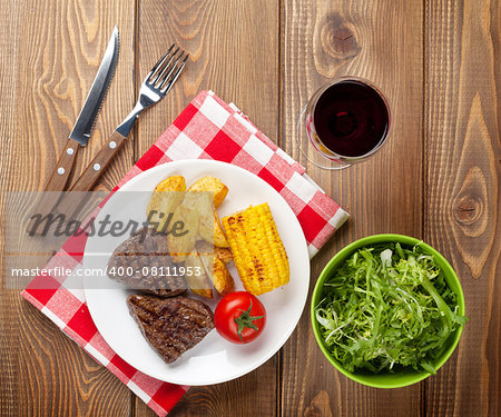 Steak with grilled potato, corn, salad and red wine on wooden table