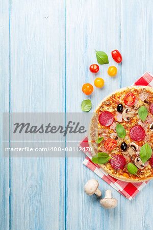 Italian pizza with pepperoni, tomatoes, olives and basil on wooden table. Top view with copy space