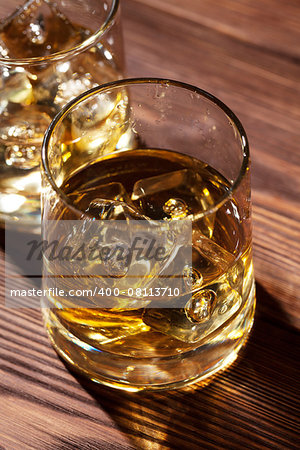 Glasses of whiskey with ice on wooden table