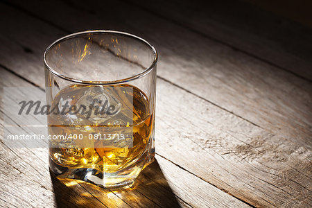 Glass of whiskey with ice on wooden table background with copy space