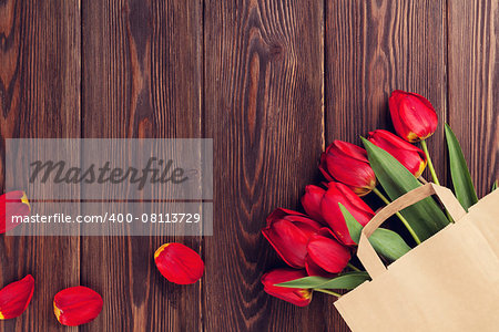 Red tulips bouquet in paper bag over wooden table background with copy space. Toned