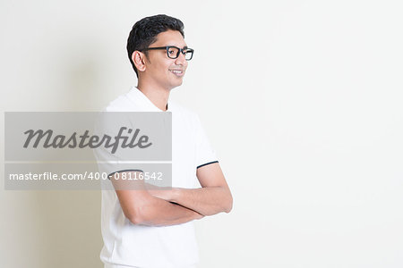 Portrait of happy Indian guy arms crossed looking at side. Asian man standing on plain background with shadow and copy space. Handsome male model.