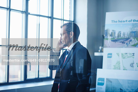 Business man chatting on smartphone whilst looking out of office window