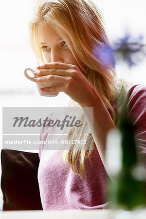 Young woman in cafe window seat drinking coffee