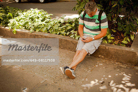 Mature man sitting on sidewalk texting on smartphone, Rio De Janeiro, Brazil