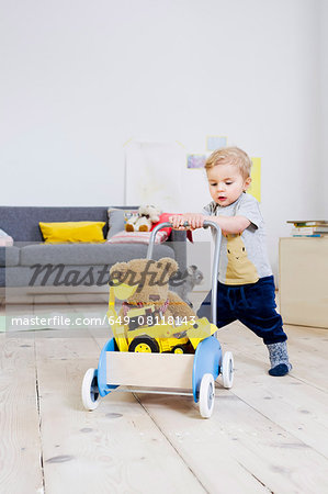 Boy pushing cart of toys at home