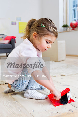 Girl sweeping floor with brush at home