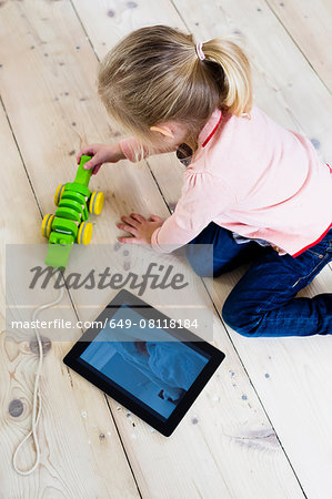 Girl with digital tablet, playing toy on wooden floor