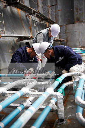 Workers checking pipework on container ship at shipyard, GoSeong-gun, South Korea