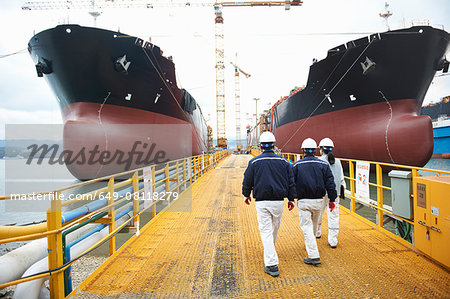 Three workers walking towards ships at shipping port, rear view, GoSeong-gun, South Korea