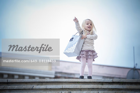 Young girl pointing from stairway carrying shopping bag, Cagliari, Sardinia, Italy