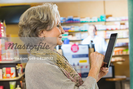 Senior woman using digital tablet to check medicine online in pharmacy