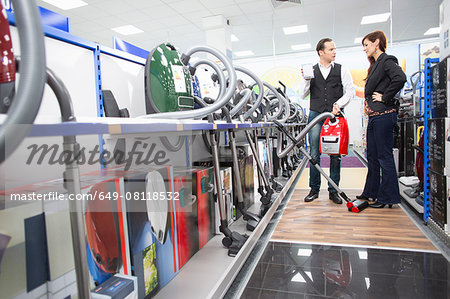 Shop assistant demonstrating vacuum cleaner in electronics store