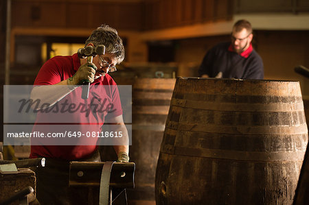 Male cooper using hammer in cooperage with whisky casks Male cooper using hammer in cooperage with whisky casks