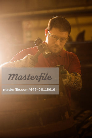 Male cooper using hammer in cooperage with whisky cask