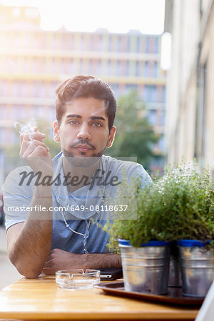 Portrait of young man outdoors, sitting at table, smoking cigarette