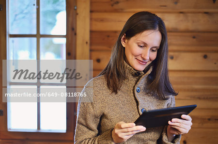 Young woman using digital tablet in log cabin, Posio, Lapland, Finland