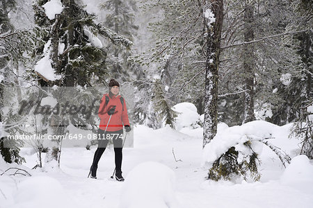 Young woman nordic walking through snow covered forest, Posio, Lapland, Finland