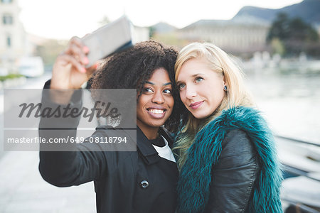 Two young women posing for smartphone selfie at Lake Como, Como, Italy