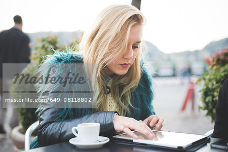 Young woman using touchscreen on digital tablet at sidewalk cafe, Lake Como, Como, Italy