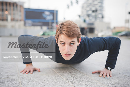 Portrait of young male runner doing push ups in city square