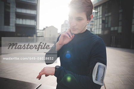 Young male runner checking neck pulse in city square