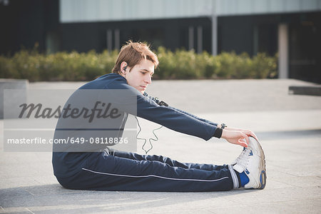 Young man touching toes in city square