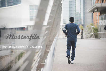 Rear view of young male runner on city footbridge