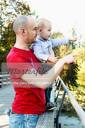 Father and son standing on bridge, looking at view, rural setting