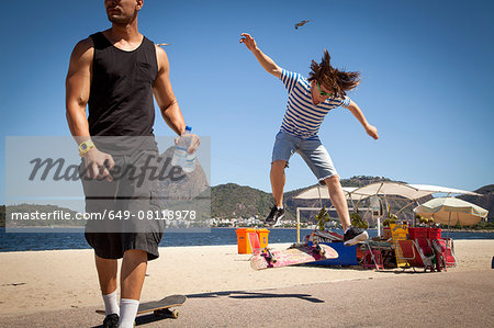 Young man doing jump on skateboard, while friend looks away