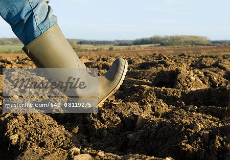 Close up of farmers rubber boot walking on ploughed field