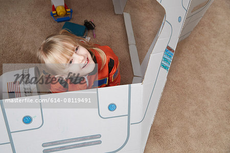 Young girl playing in cardboard spaceship, wearing astronaut outfit, elevated view