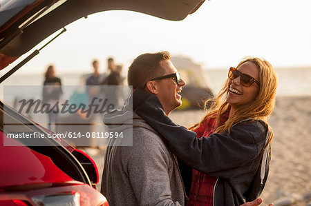Couple relaxing behind vehicle on beach