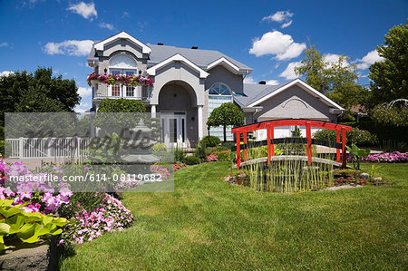 Grey brick cottage style residential home and landscaped  manicured garden with red footbridge, Quebec, Canada