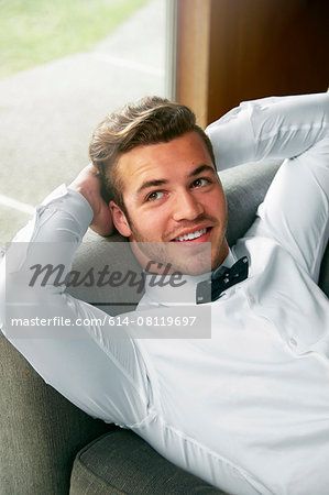 Portrait of man wearing bow tie reclining on sofa with hands behind head