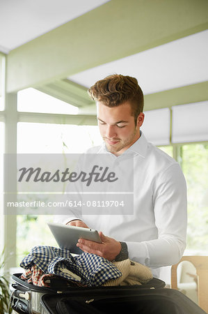 Businessman packing suitcase at home reading digital tablet