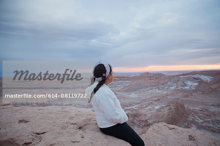 Young girl sitting on rock looking at view, Valley of the Moon, San Pedro. Atacama. Chile