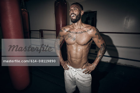 Tattooed male boxer with hands on hips laughing in gym